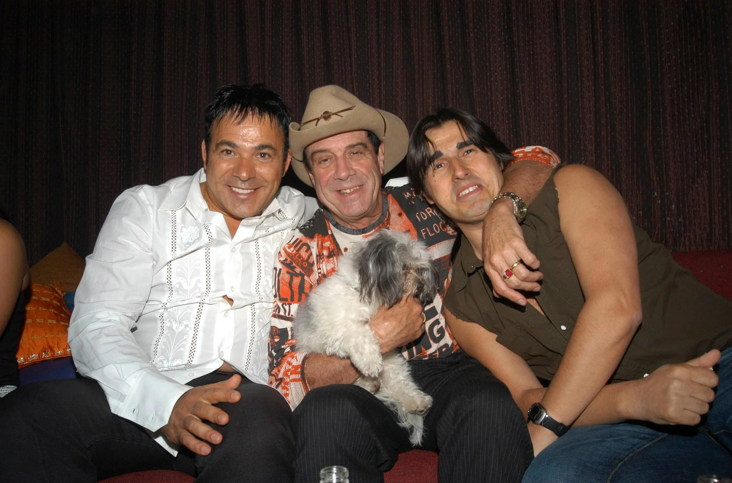 The three men with their arms around each other on a couch in a club