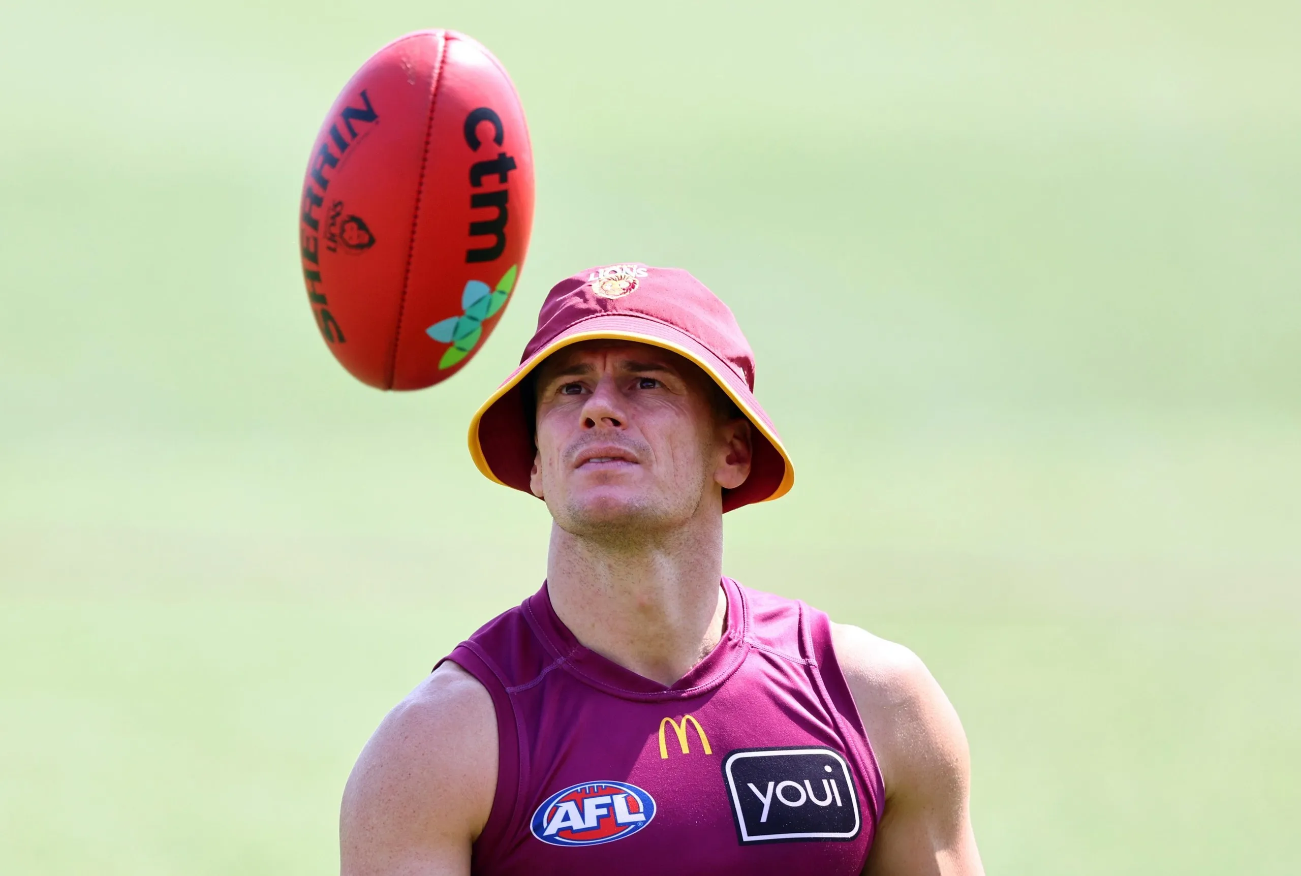 Dayne Zorko of the Brisbane Lions in a bucket hat looking at a football in mid-air during a training session