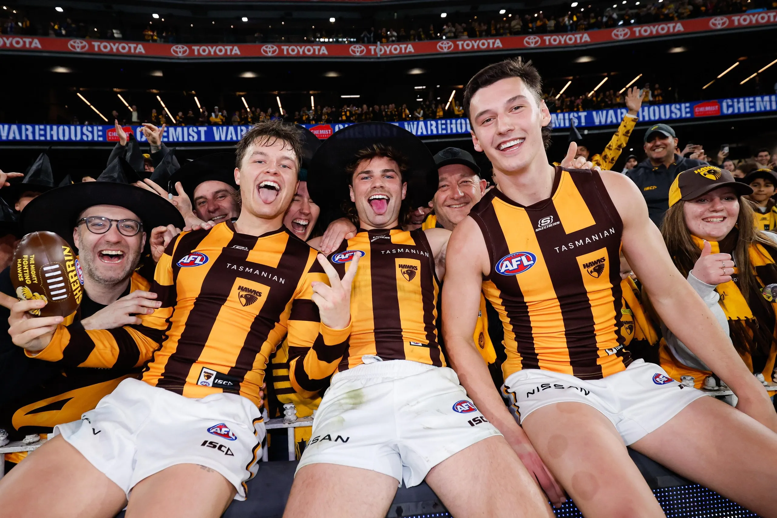 Jack Ginnivan, Nick Watson in a wizard hat, and Connor Macdonald pose for a photo with fans at the MCG after winning their elimination final in 2024